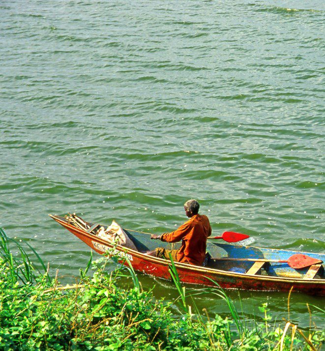 fishing on the Kazinga Channel in Uganda, surrounded by lush vegetation and calm waters, with hippos and birds in the background.