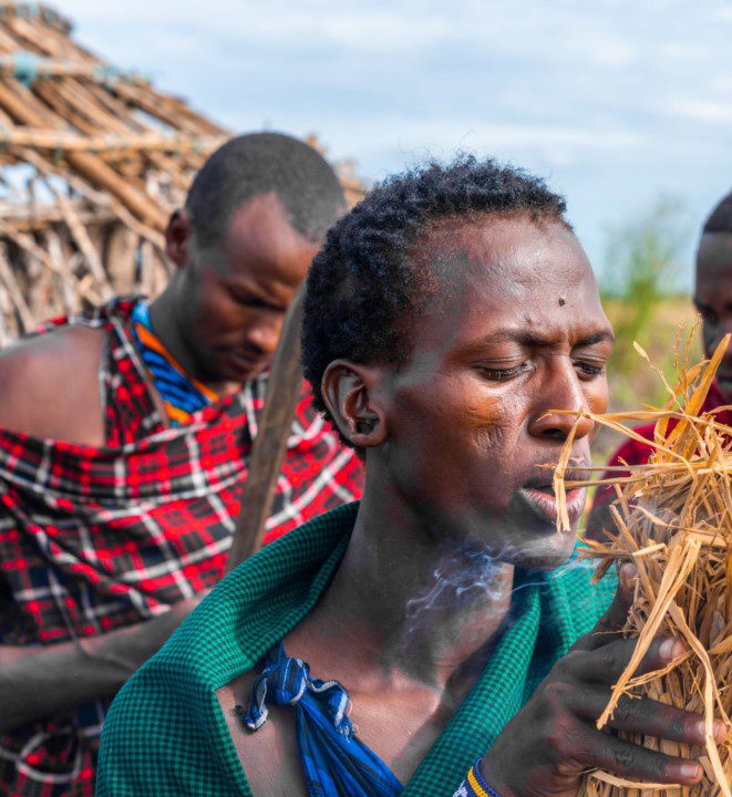 A traditional healer in Tanzania performing a spiritual ritual with fire, using herbs and cultural tools.